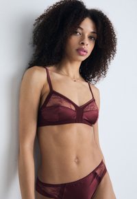 Set di lingerie in satin borgogna composto da un bralette con pannelli in pizzo e spalline regolabili, abbinato a un perizoma con dettagli in pizzo coordinati.