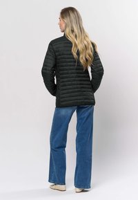 Svart quiltad jacka med ståkrage, med vertikala sömmar och en figurnära silhuett, bärs över vida blå jeans.