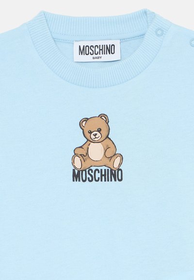 Sweatshirt de bebé azul claro com decote canelado, apresentando um gráfico de urso de peluche em cartoon e o texto "MOSCHINO" abaixo em preto.