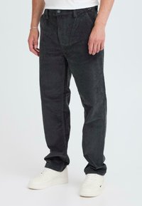 Black corduroy pants with vertical ribs, a button closure, belt loops, and side pockets, paired with white sneakers.