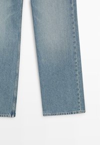 Jean en denim bleu clair avec jambes droites et coutures visibles le long des coutures, posé à plat sur un fond blanc.