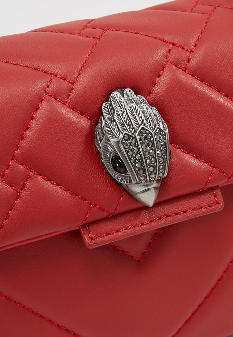 Czerwona torebka z pikowanej skóry z metalowym zapięciem w kształcie ptaka ozdobionym czarnymi kamieniami. Gładka faktura z kontrastującymi detalami przeszyć.