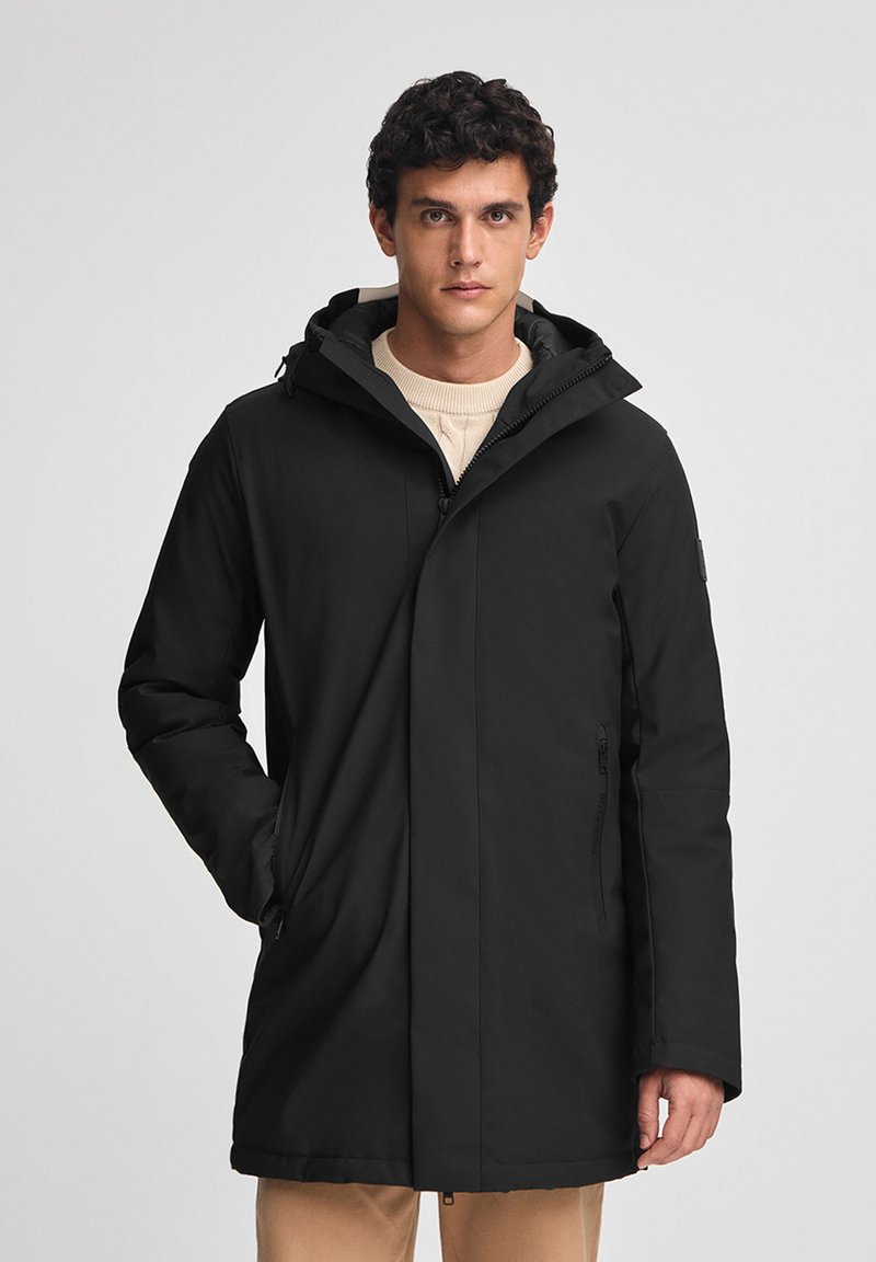Parka nera impermeabile con cappuccio, dotata di zip frontale, due tasche laterali e una silhouette snella. Tessuto dal tocco liscio.