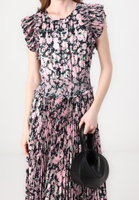 Kukallinen mekko, jossa on röyhelöhihoja, smockattu yläosa ja vuorattu hame vaaleanpunaisena, mustana ja vihreänä. Yhdistetty mustan nahkakäsilaukun kanssa.