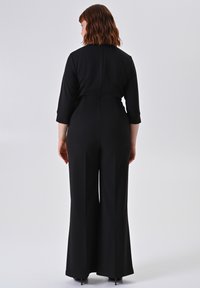 Salopette nera con maniche a tre quarti, vita aderente e pantaloni a gamba larga. Tessuto morbido con una texture liscia e dettagli minimi.