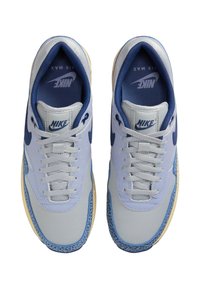 Ljusblå Nike Air Max sneakers har en meshtopp med marinblå accenter, vadderad krage och strukturerad gummisula. Snörena är framträdande.