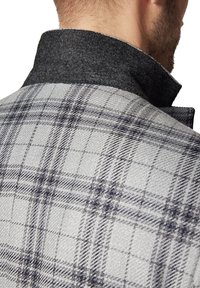 Kołnierz szarej i czarnej marynarki w kratę, z teksturowanym materiałem, kontrastującym ciemnym kołnierzem z filcu i subtelnym wzorem w kratkę.