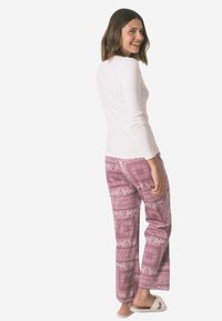 Maglietta bianca a maniche lunghe abbinata a pantaloni rosa con motivo floreale e geometrico. Modella che indossa sandali, girata di lato.