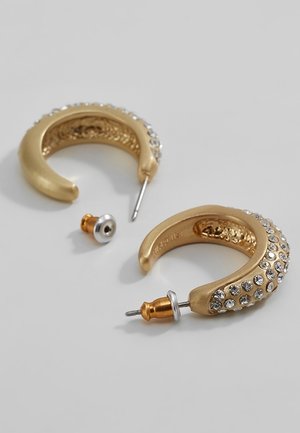 Paar gouden halvemaanvormige creolen met heldere strass-steentjes en metalen pennen met vlinderbevestigingen op een witte ondergrond.