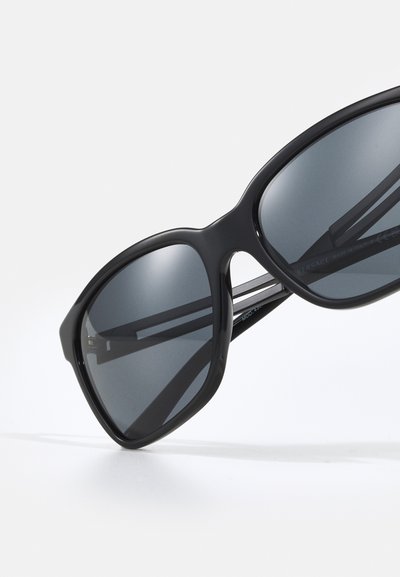 Ochelari de soare negri cu o ramă din plastic elegantă și lentile întunecate. Prezintă o formă distinctivă și un branding proeminent Versace pe frunte.