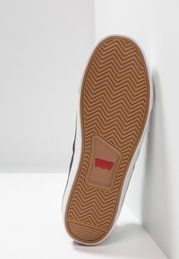 Musta tennarikenkien pohja kalanruotokuvioilla, valkoiset sivukoristeet, punainen Levi's-logo ja ruskea kumipohja.