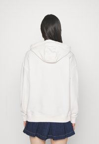 White hooded sweatshirt with a relaxed fit. Soft texture, dropped shoulders, ribbed cuffs, and hem. Paired with a dark pleated skirt.