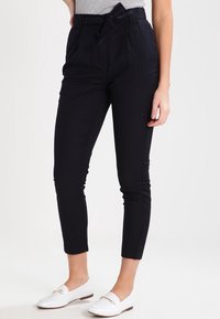 Marina randiga byxor med hög midja, knytbälte, avsmalnande ben och slät tygkvalitet, i kombination med vita slip-on skor.