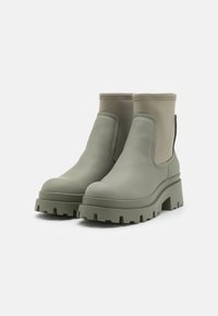 Botines de piel verde con suela gruesa, que presentan una textura suave y paneles laterales elásticos. El tacón es grueso y escalonado.