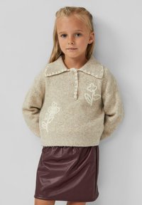 Beige gebreide trui met een geschulpte kraag en bloemenborduurwerk, gecombineerd met een diep bordeaux faux-leer rok met een geraffineerde taille.