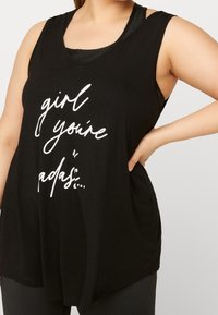 Svart ärmlös tanktop i mjuk bomull med avslappnad passform, med vit tryckt text: "tjej, du är grym..." på framsidan.