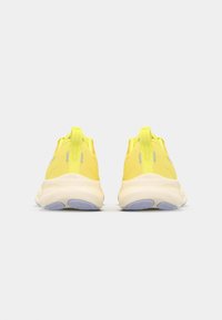 Baskets de sport jaunes avec une tige en maille respirante, une semelle amortissante et un onglet arrière en cuir texturé. Présente une semelle extérieure en caoutchouc violet.