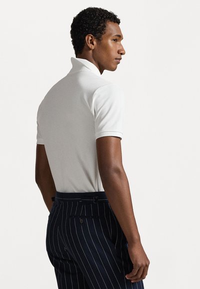 Hvit polo skjorte med kort krage, tettsittende design. Kombinert med marineblå stripete bukser med knapp og beltedetalj.