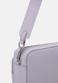 Borsa in pelle viola di forma rettangolare, con una cerniera argentata e una tracolla testurizzata e regolabile per il trasporto.