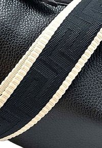 Zwarte leren tas met een gestructureerd oppervlak, voorzien van een zwart-wit gestreepte schouderband. De band heeft een verhoogd geometrisch ontwerp en een geribbelde rand.