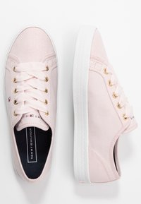 Světle růžové plátěné tenisky s bílou gumovou podrážkou, zlatými dírkami na tkaničky a odpovídajícími růžovými tkaničkami. Logo viditelné na boku a na jazyku.