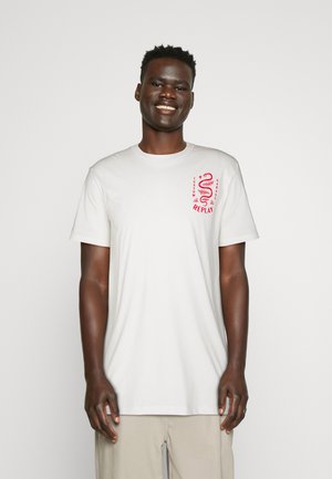 Camiseta de algodón blanca de manga corta, con un diseño gráfico rojo en la parte superior izquierda del pecho que muestra la palabra "REPLAY" y elementos decorativos.
