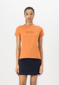 Short-sleeve orange T-shirt with a subtle "BOSS" logo printed in a slightly darker shade, paired with a dark blue skirt.