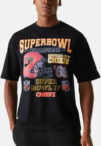 T-shirt noir avec un motif graphique coloré comprenant "Champions du Super Bowl", le logo des Kansas City Chiefs et un casque de football dans un style vintage.