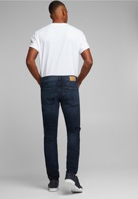 Mörkblå smala jeans i denim, med en brun läderpatch på baksidan av midjan och subtila sömdetaljer.