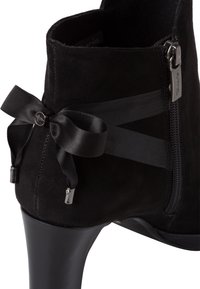 Botte noire en daim à la cheville avec fermeture éclair, accentuée par un nœud en satin et des bandes élastiques noires autour du haut. Design à talon haut.