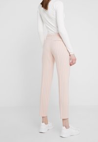 Pantalon rayé rose pâle avec une coupe fuselée, taille élastique et poches arrière, porté avec des baskets blanches.
