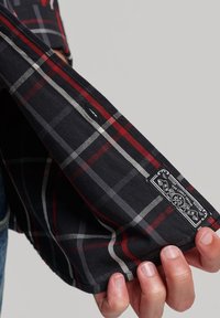 Camicia a maniche lunghe a quadri neri e rossi con accenti grigi, in cotone, con etichetta sulla manica e dettaglio con bottone sul polsino.