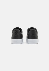 Sneaker nere con tacchi texturizzati e suole bianche. La parte posteriore presenta un logo e dettagli a motivo nell'area del tallone. Materiale superiore liscio.