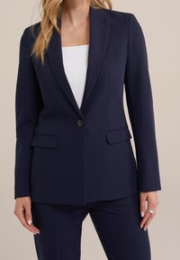 Námořnický oblekový blejzr ve hladkém materiálu s jedním knoflíkem, klopami a dvěma předními kapsami; slim fit střih.