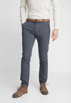 Pantalones gris ajustados hechos de una tela texturizada, combinados con un cinturón de cuero marrón y zapatos de ante marrón, con un diseño de corte ajustado.