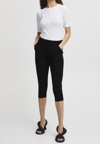 Černé krátké kalhoty s páskem na stažení, bočními kapsami a přiléhavými manžetami, zkombinované s bílým topem s krátkým rukávem a černými sandály na podpatku.