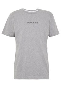 Camiseta de algodón gris con cuello redondo, mangas cortas y un logo negro "CALVIN KLEIN JEANS" impreso en el pecho. Textura suave.