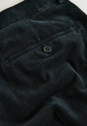 Melnas korduroja audumam ar rievotu tekstūru, ar vienu aizmugures kabatu un apaļu tumšu pogu aizdarē.