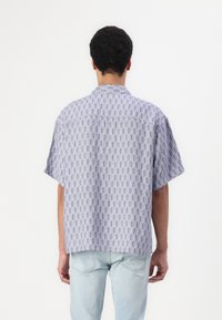 Camisa de manga corta hecha de tela estampada en tonos de azul, con un corte relajado y un cuello con solapa, detalles de costura visibles.