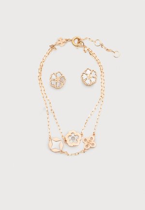 Pulsera de doble cadena dorada con dijes en forma de flor y estrella, acompañada de pendientes de botón a juego con diseño de flor sobre fondo blanco.