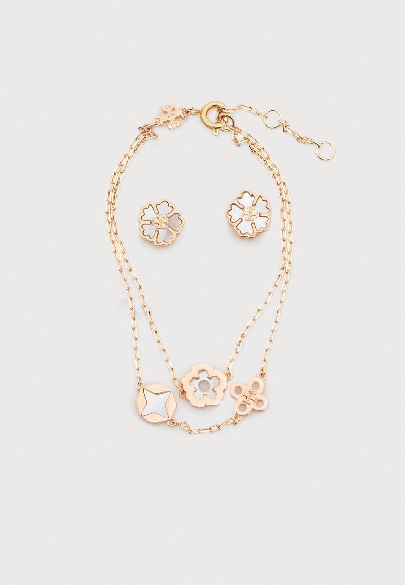 Βραχιόλι διπλής αλυσίδας σε χρυσό χρώμα με κρεμαστά κοσμήματα σε σχήμα άνθους και αστεριού, συνοδευόμενο από σκουλαρίκια καρφάκια με αντίστοιχο σχέδιο άνθους, σε λευκό φόντο.