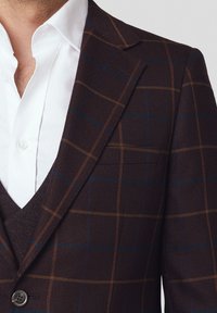 Brązowy marynarka w kratę z teksturowanej tkaniny, z niebieskimi i pomarańczowymi paskami. Połączona z białą koszulą pod spodem.