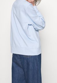 Sudadera azul claro con un corte relajado, que presenta un escote redondo y dobladillo acanalado. Combinada con una falda de mezclilla oscura, ligeramente acampanada en la parte inferior.