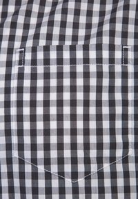 Tissu à carreaux noir et blanc avec une poche carrée cousue au centre, assortie au motif et avec des coutures le long des bords.