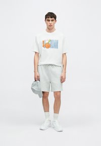 Fehér póló színes "AIR JORDAN" grafikával, szürke sportnadrág, szürke sapka és fehér tornacipő. Hétköznapi sportos öltözék.