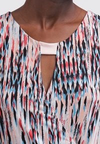 Haut cache-cœur multicolore en tissu doux, présentant des motifs abstraits bleus, rouges et noirs, avec un décolleté en forme de goutte d'eau et des manches courtes.