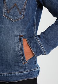 Jeansjacka med blå tvätt, detaljstickningar och en framficka. Strukturerad tyg med en slim fit-design.