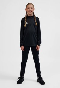 Zwart sportpak met een langarmtop met ritssluiting en taps toelopende broek. Het materiaal is glad, met een nauwsluitend ontwerp en subtiele logodetails.