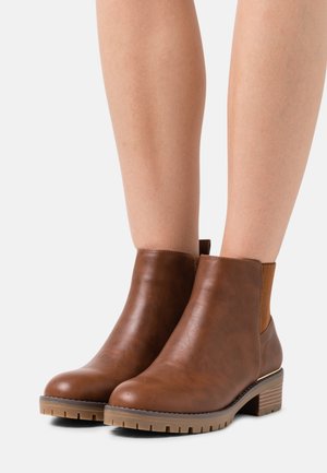 Botas de tobillo marrones hechas de cuero suave, con paneles laterales elásticos, punta redondeada y una suela sintética texturizada con un tacón bajo.
