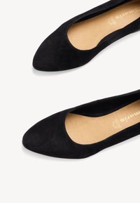 Ballerines en suède noir avec un bout pointu et un design de découpes arrondies à l'avant. L'intérieur révèle une semelle intérieure beige.